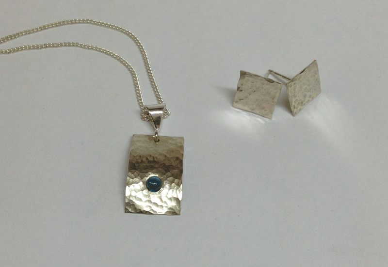 Blue topaz set in hammered sterling silver with companion stud earrings. Comes with an 18" sterling silver chain. Studs are ~10mm.  $80 or 1 lucky raffle ticket. 